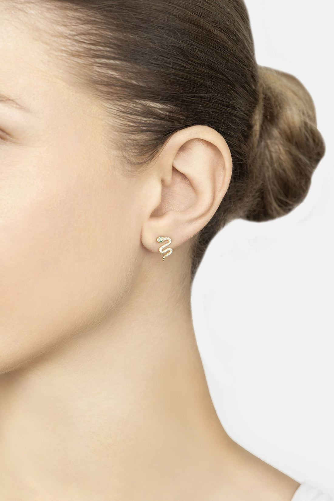 Small gold snake stud earring with green eye on side ear