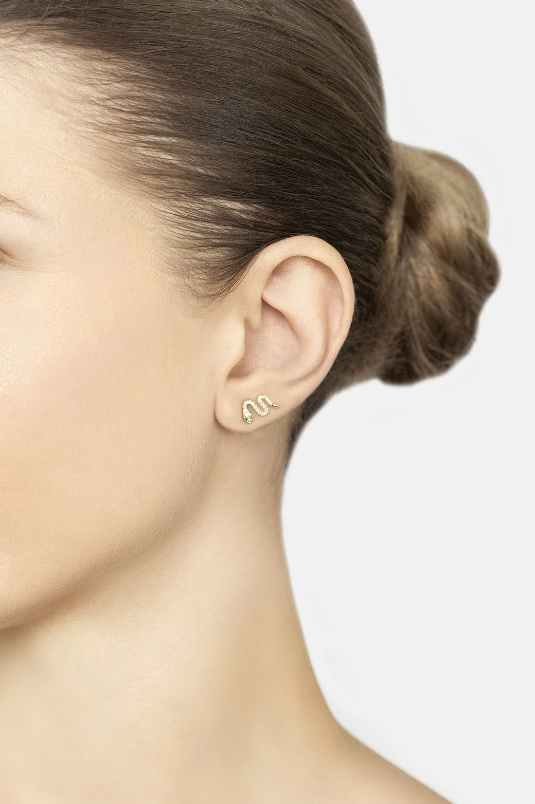 Gold snake stud earring with green eye, worn on ear