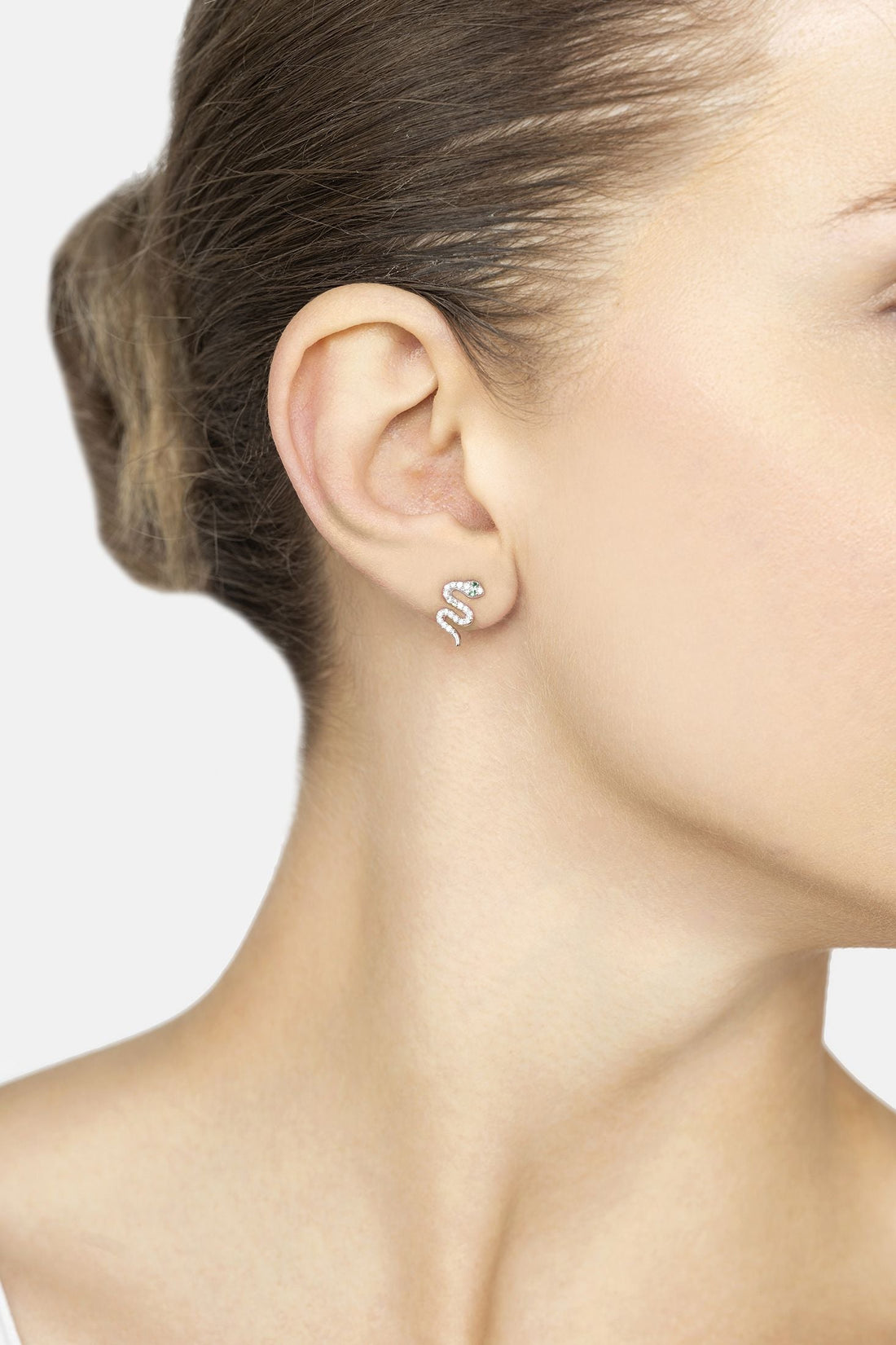 Silver snake stud earrings with small green CZ accent, worn on ear