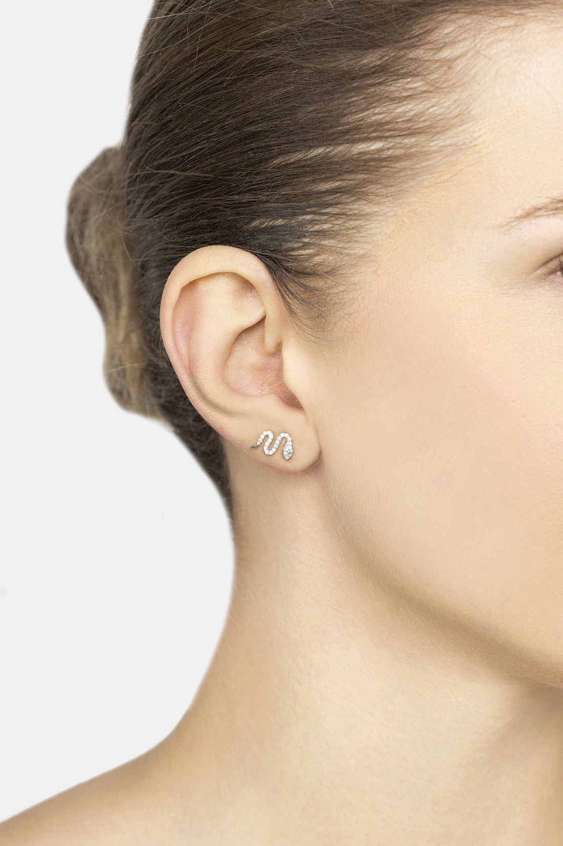 Silver snake stud earrings with green CZ accent, close-up side view on ear