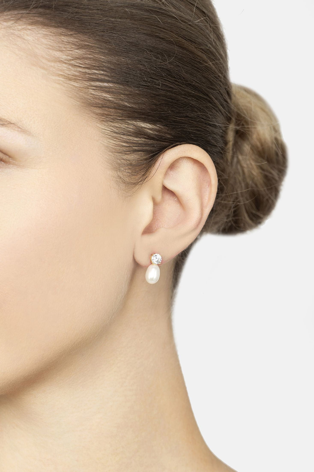 Gold earrings on ear: round sparkle stud with white pearl teardrop drop