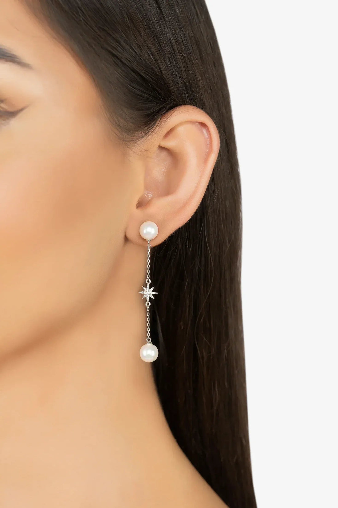 Pearl drop earrings dangling from ear with star charm and silver chain