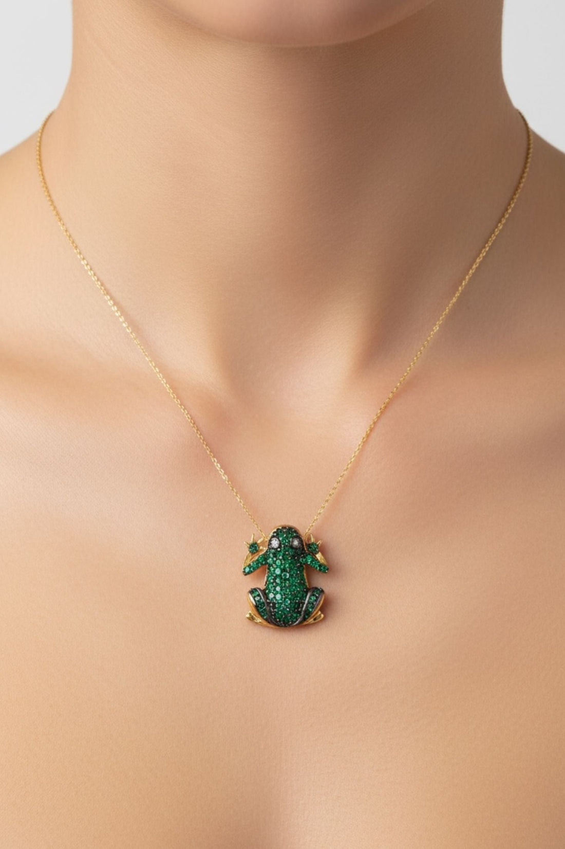 Gold frog pendant necklace worn on chest; green and blue-toned enamel