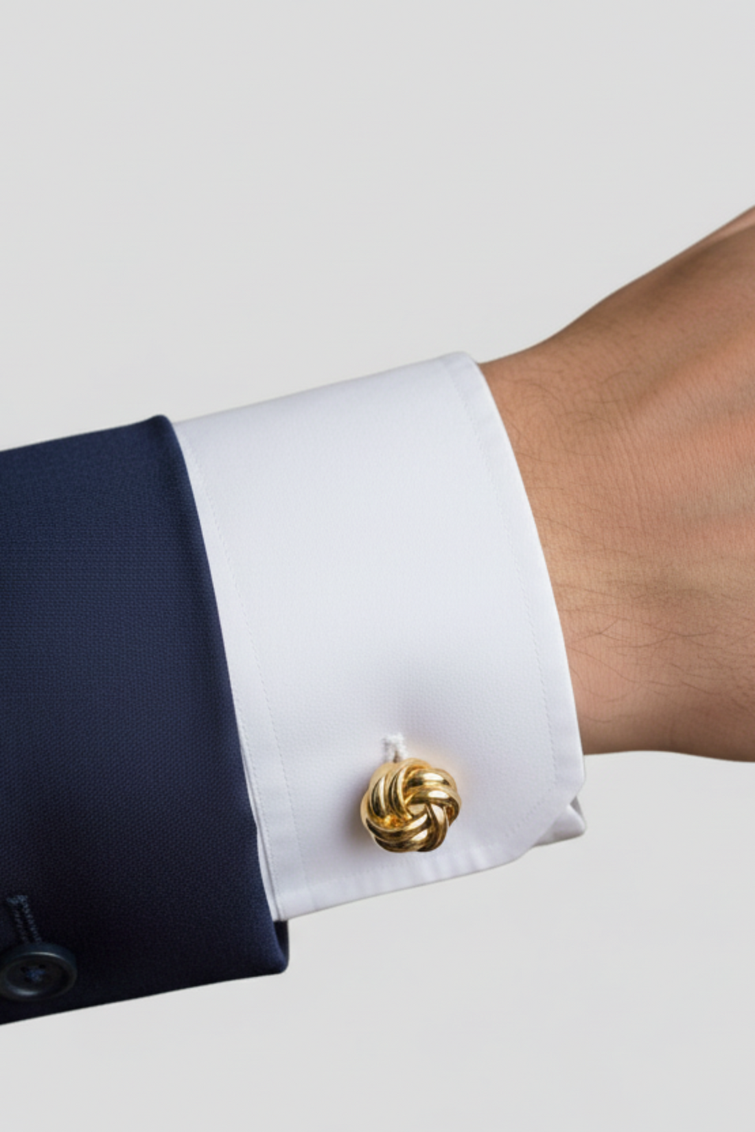 Gold-tone knot cufflink fastened on a white dress shirt cuff