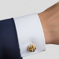 Gold-tone knot cufflink fastened on a white dress shirt cuff