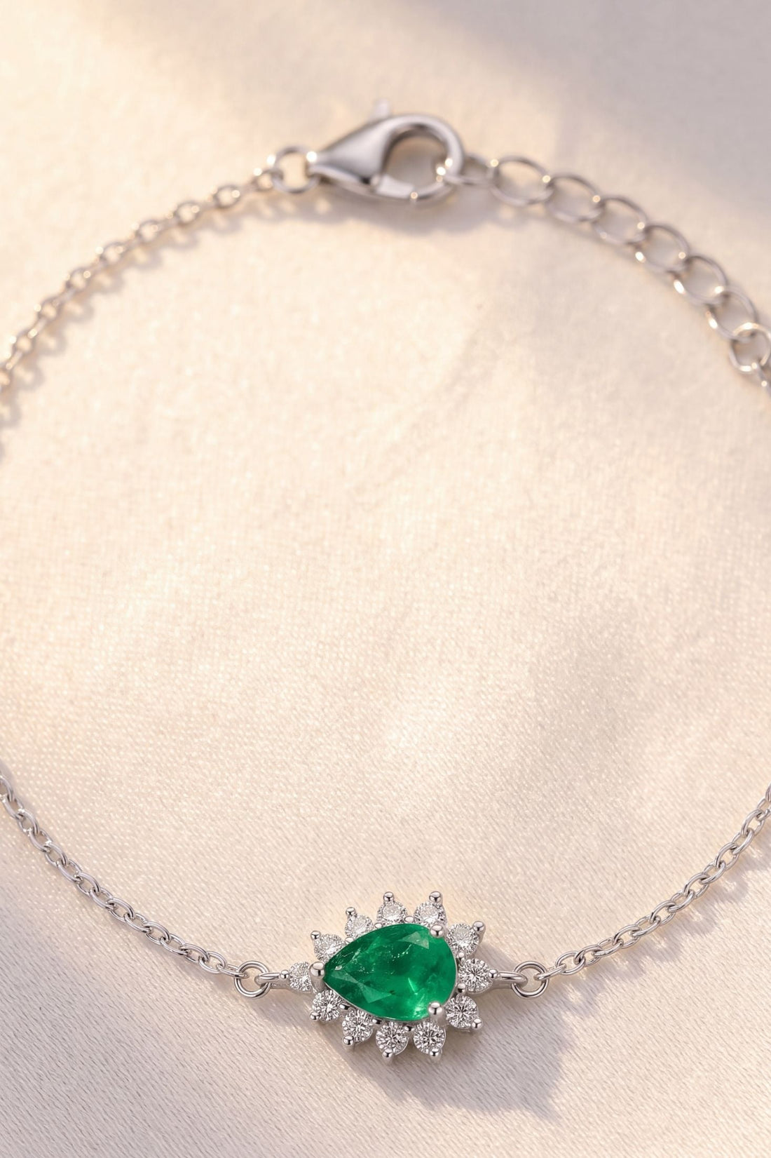 Close-up silver bracelet with emerald-green oval gemstone and starburst crystals