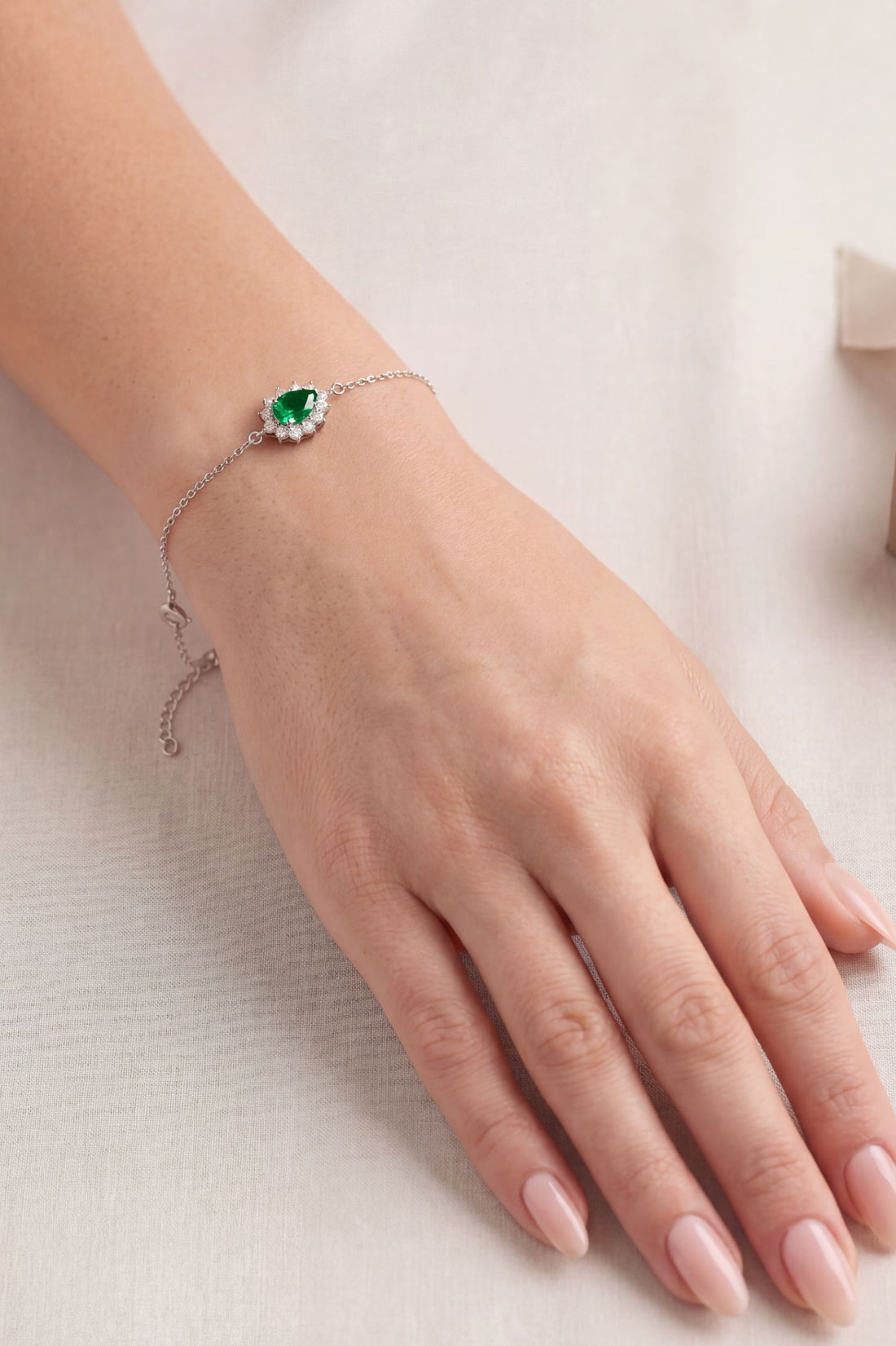 Silver bracelet on wrist with emerald-green oval gemstone and crystal halo