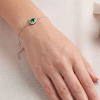 Silver bracelet on wrist with emerald-green oval gemstone and crystal halo