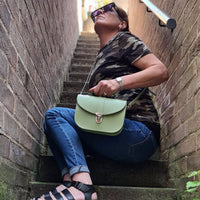 Sage green leather flap bag worn crossbody with adjustable strap