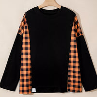 Black long-sleeve top on hanger with orange plaid sleeve panels