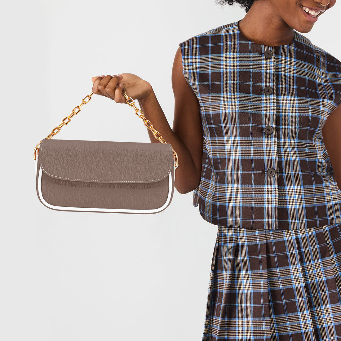 Brown leather shoulder bag with front flap and gold chain strap, held by hand