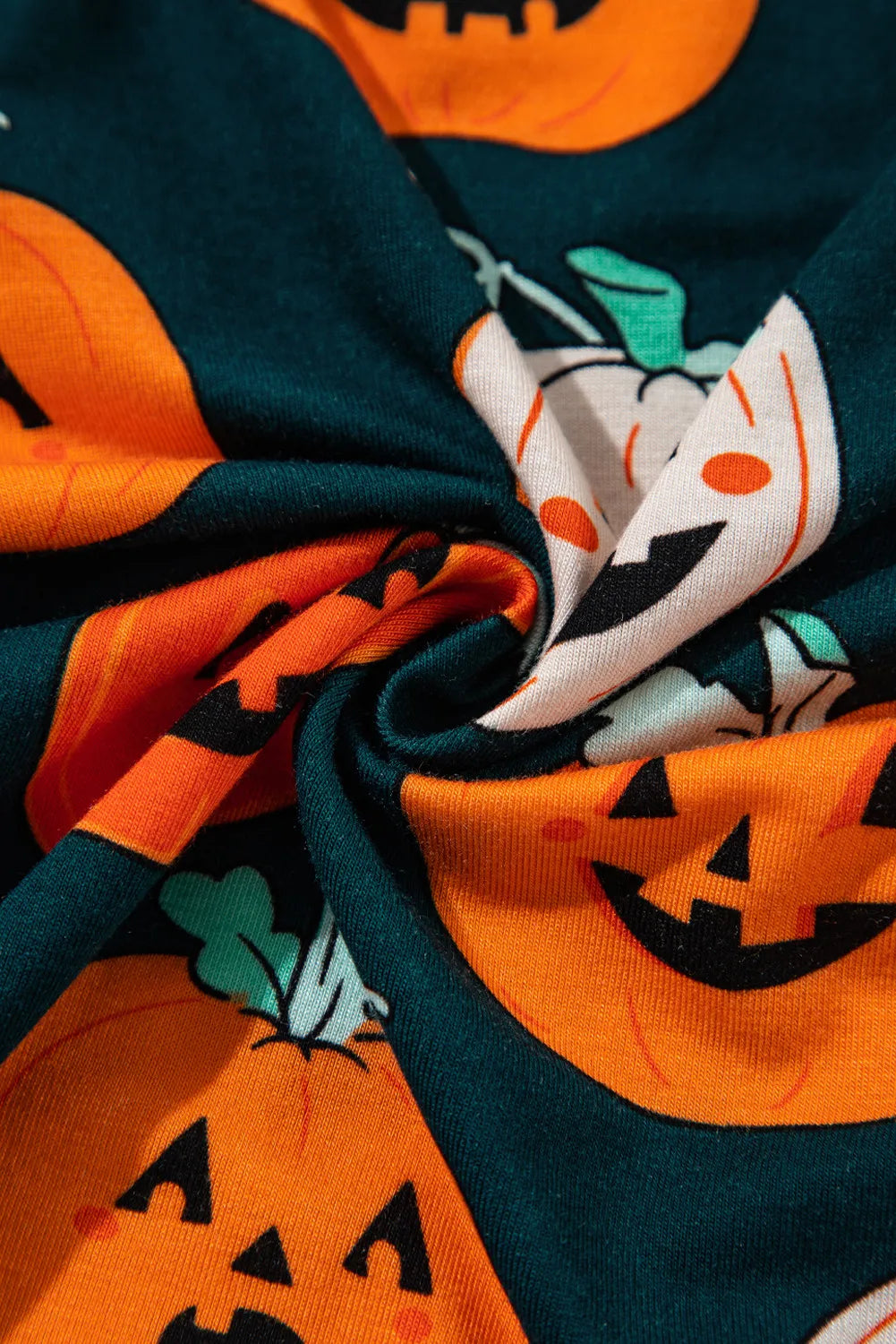 Close-up fabric with dark green and orange pumpkin print and jack-o&
