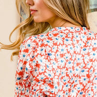 Orange floral V-neck top back view with smocked puff sleeves, blue-and-white print
