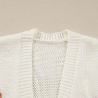 Close-up of off-white knit cardigan with open front and pumpkin embroidery patch.