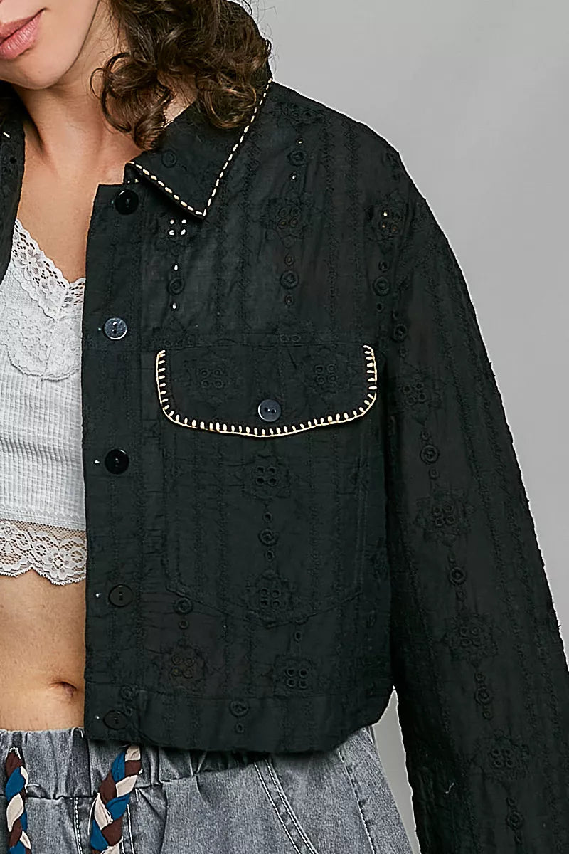 Close-up of black cropped button-front eyelet cotton jacket: button placket and flap pocket details.