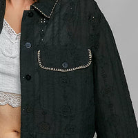 Close-up of black cropped button-front eyelet cotton jacket: button placket and flap pocket details.