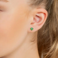 Emerald-green heart stud earrings on ear with small silver posts
