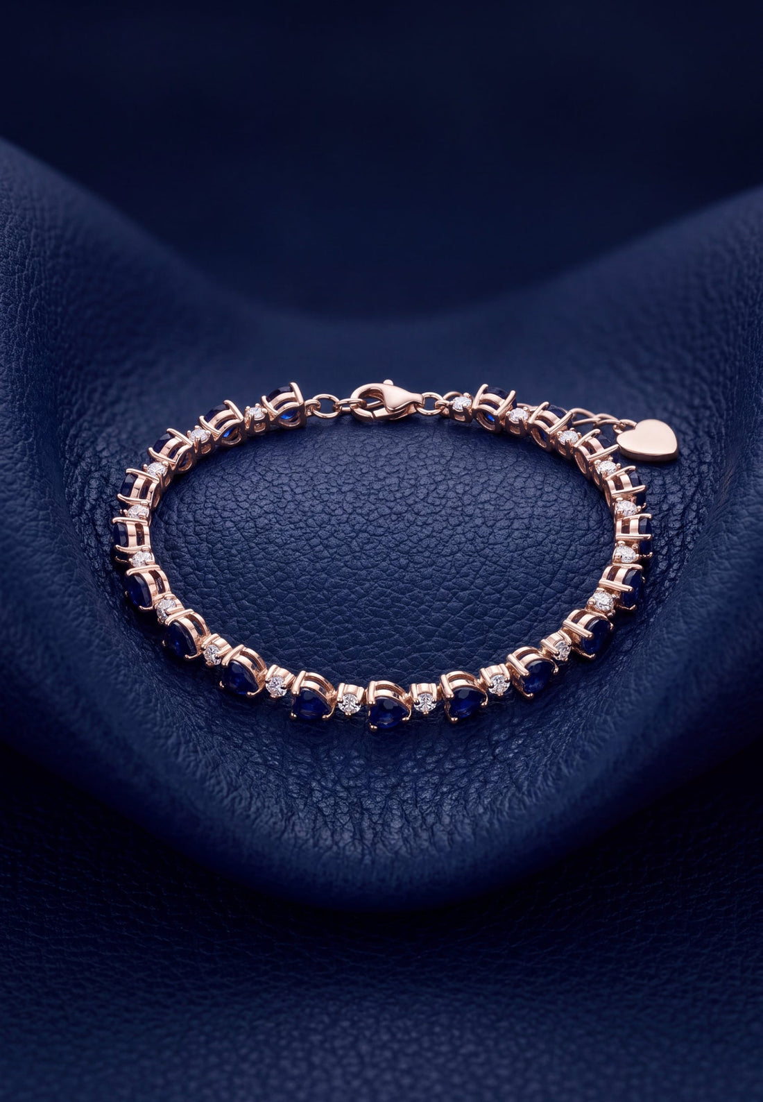 Gold-tone tennis bracelet with blue faceted stones and heart-shaped clasp charm