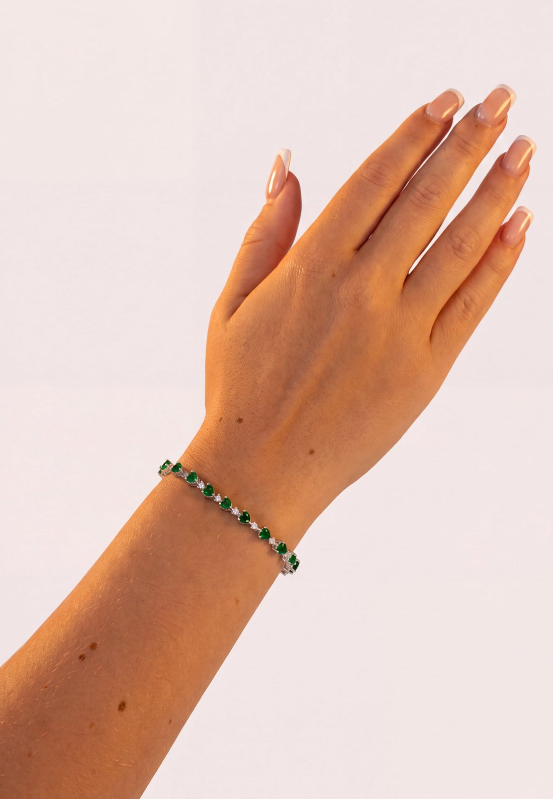 Green heart tennis bracelet on wrist, silver chain with small link design