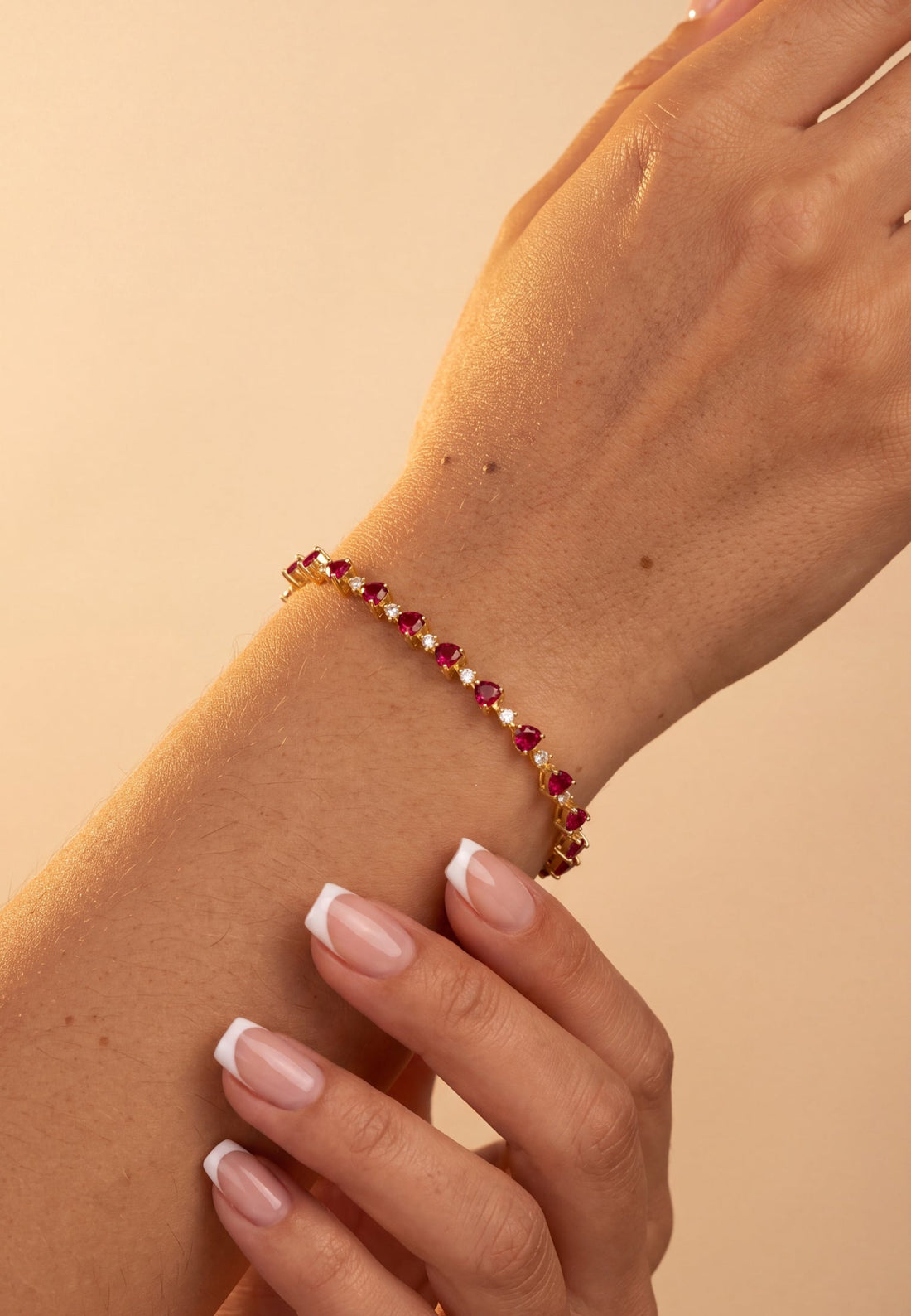 Gold-tone heart tennis bracelet with ruby-pink heart stones on forearm