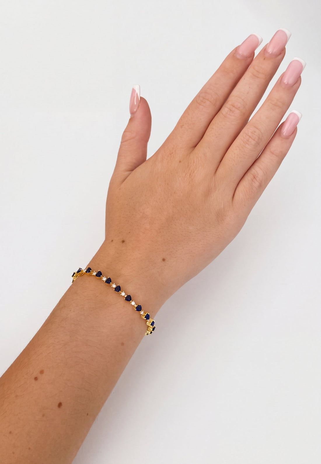 Gold-tone tennis bracelet with blue faceted stones on an open hand