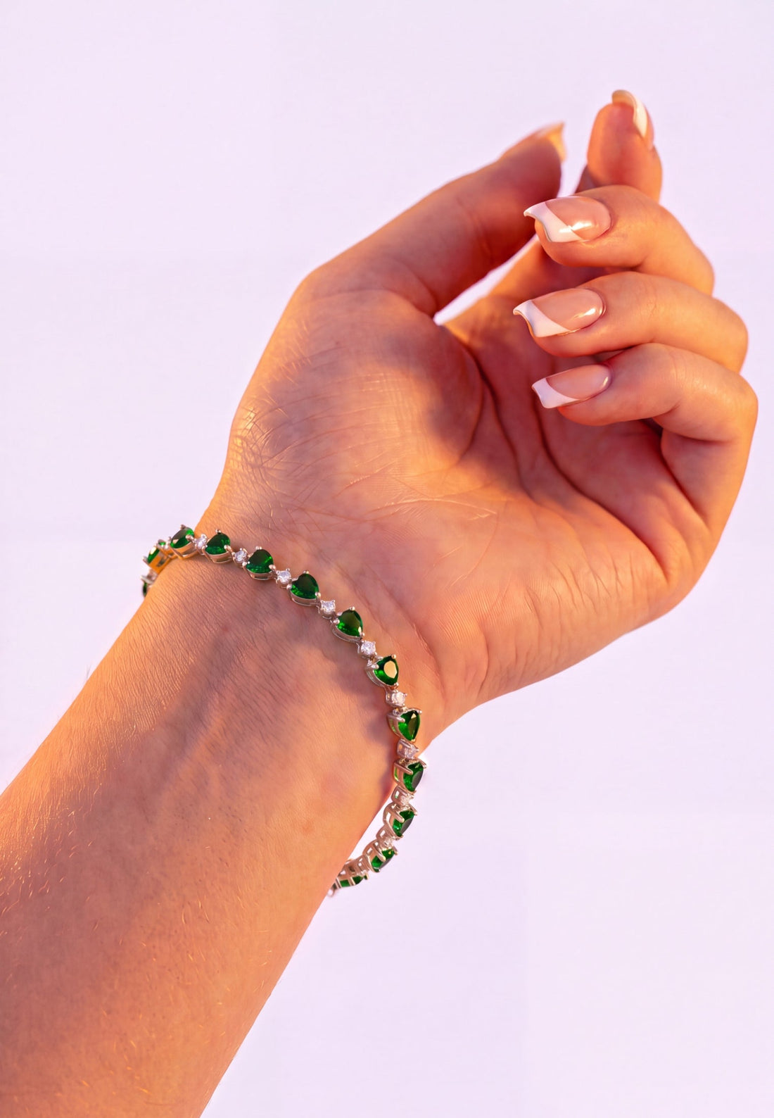 Green heart tennis bracelet on hand, silver chain with emerald-cut stone hearts