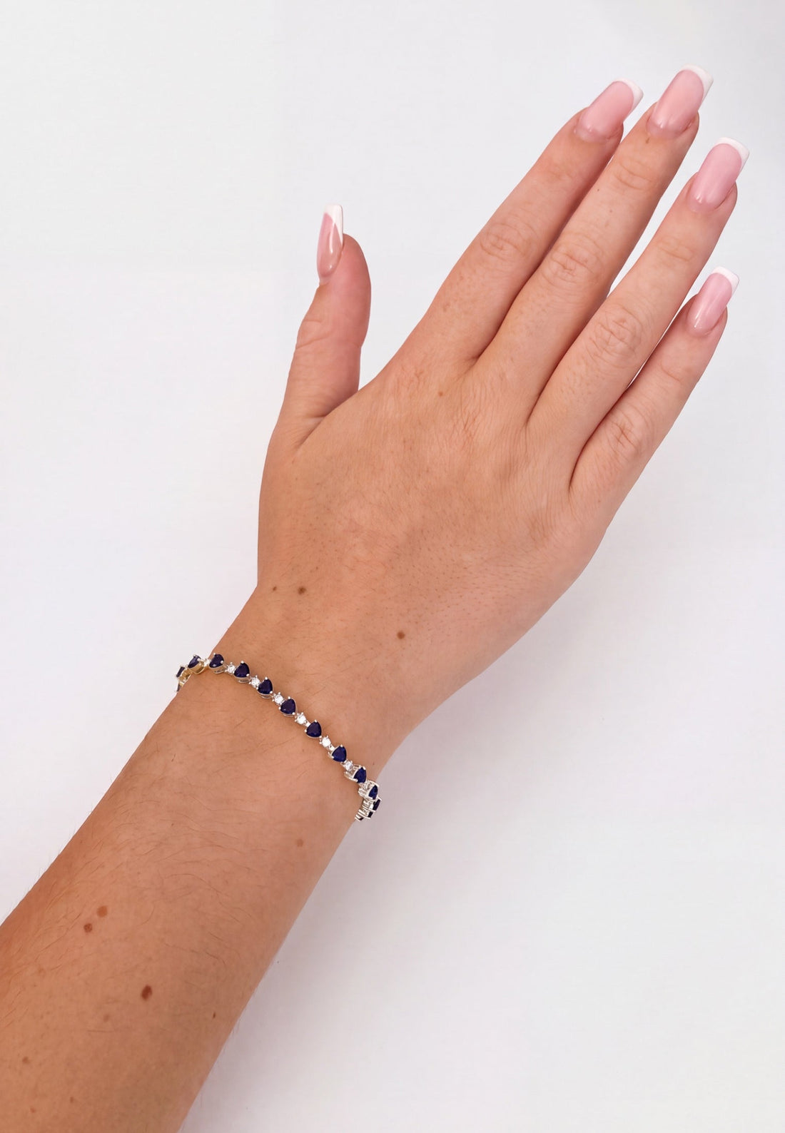 Silver tennis bracelet with blue heart-cut gemstones on raised hand