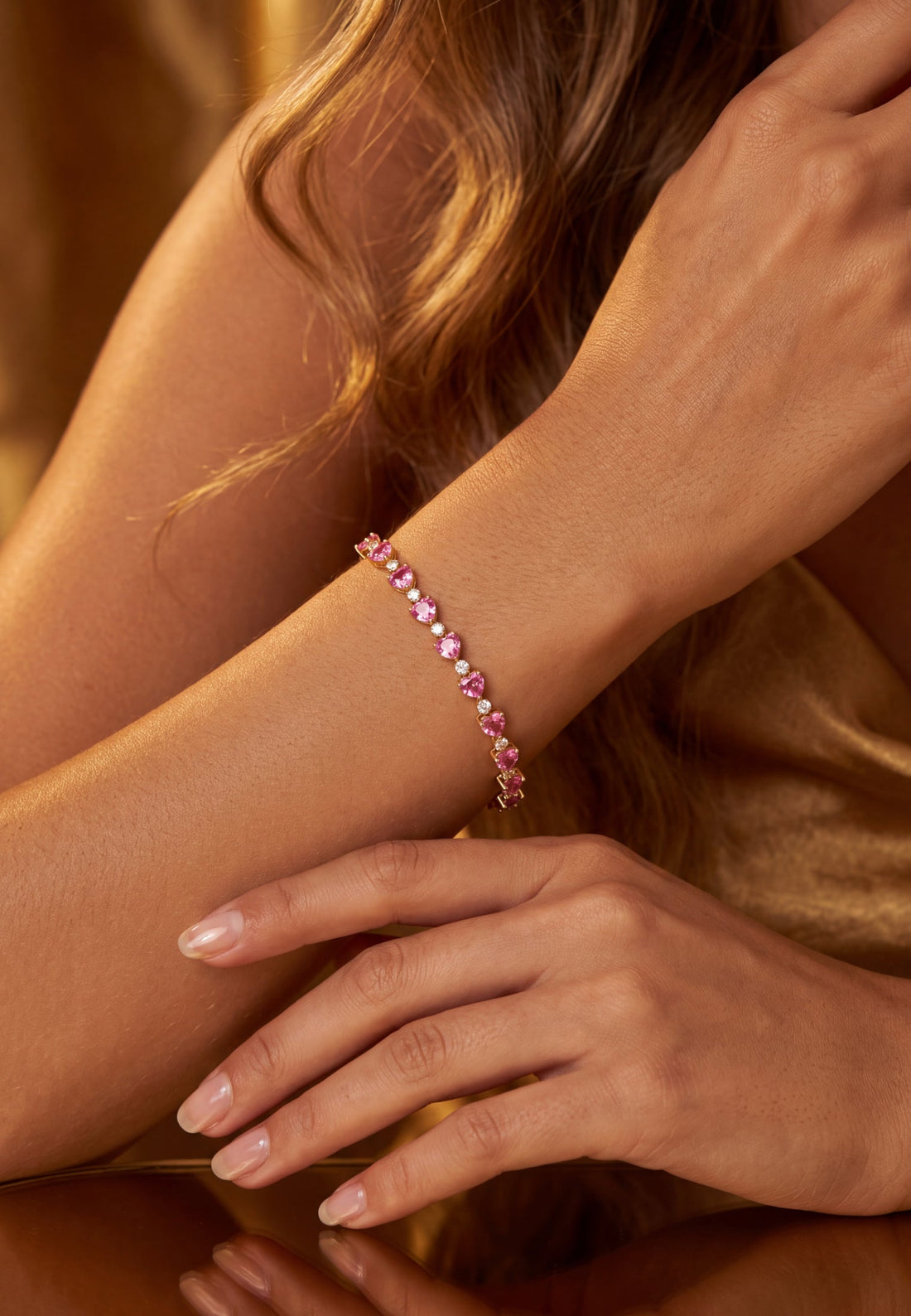 Gold-tone heart-stone tennis bracelet on wrist with pink ruby hearts in links