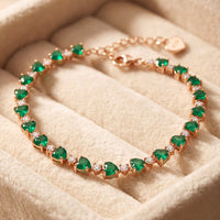Rose gold bracelet featuring green emerald-cut heart stones in a tennis row