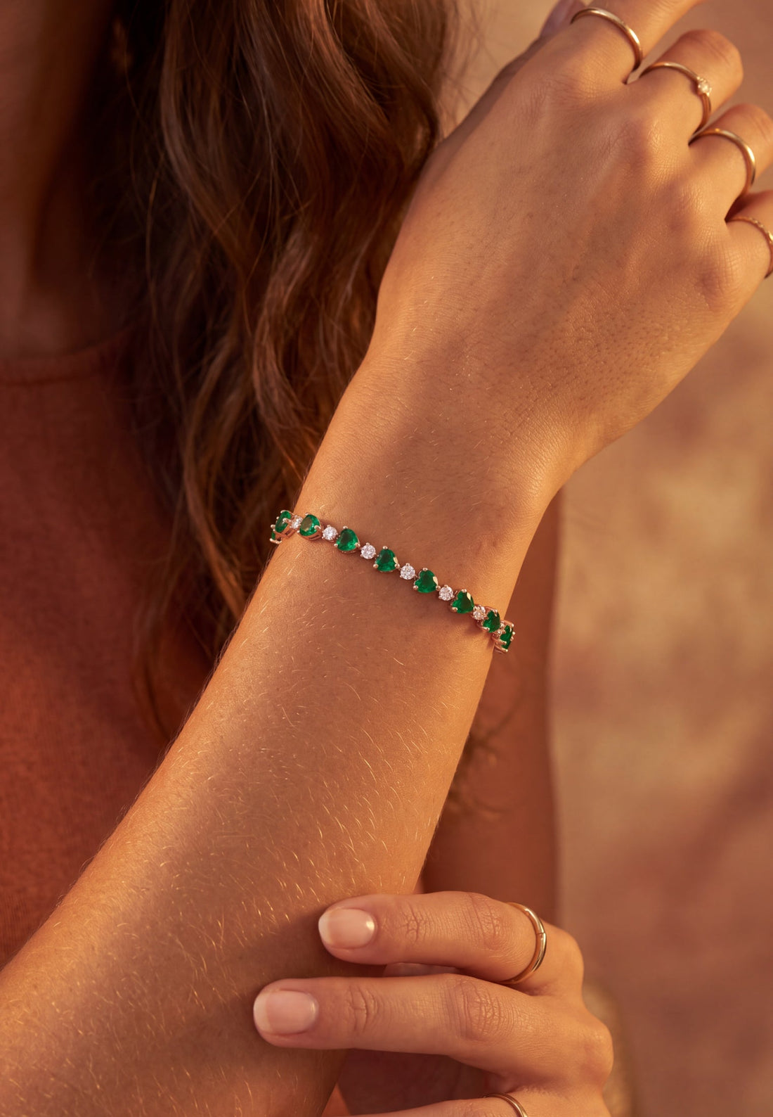 Rose gold tennis bracelet with green emerald-cut heart stones on the wrist