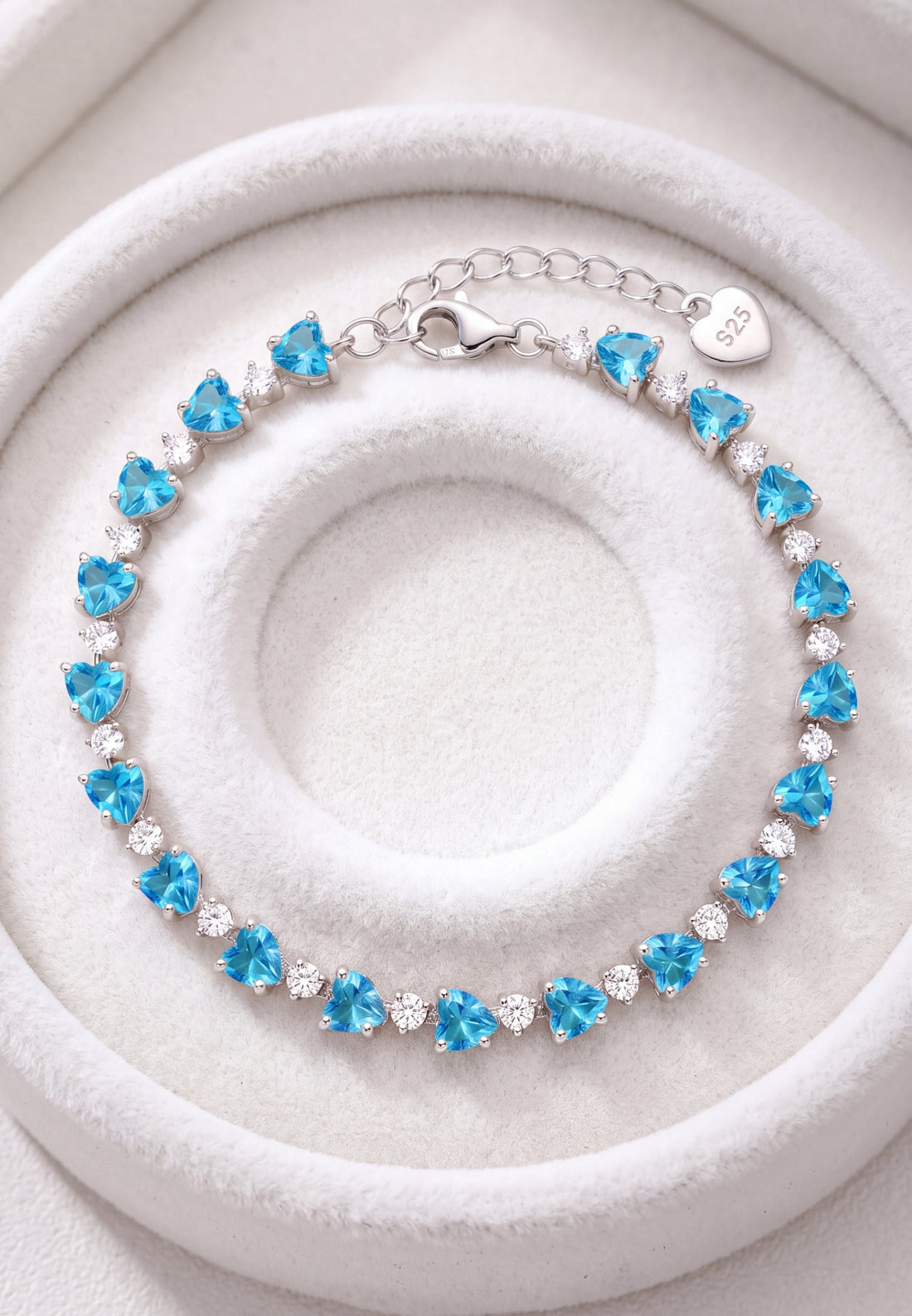 Silver heart-cut blue topaz tennis bracelet on white jewelry cushion