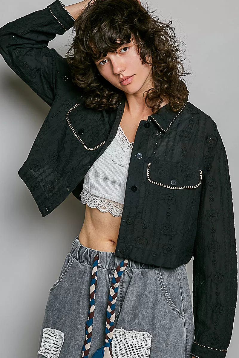 Black cropped eyelet cotton jacket with button placket, pointed collar, and stitched flap pockets.