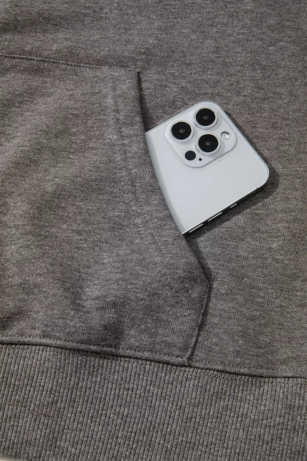Dark gray hoodie sleeve and pocket area with ribbed cuff; smartphone beside