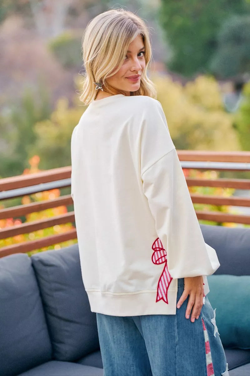 Cream sweatshirt back view with red bow graphic and blue bow patch on the sleeve.