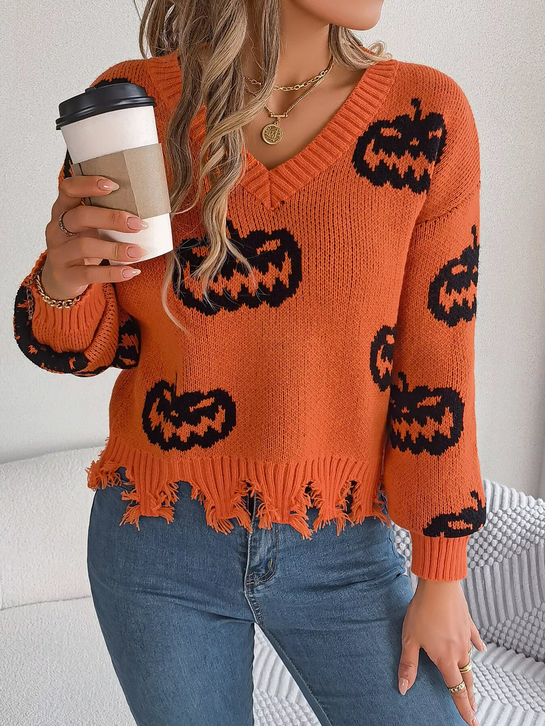 Orange knit V-neck sweater with black pumpkin pattern and fringe-style distressed hem