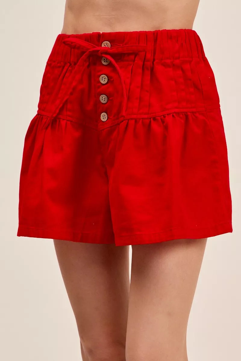 Red denim shorts with pintucked elastic waist, button placket, and waist tie detail.