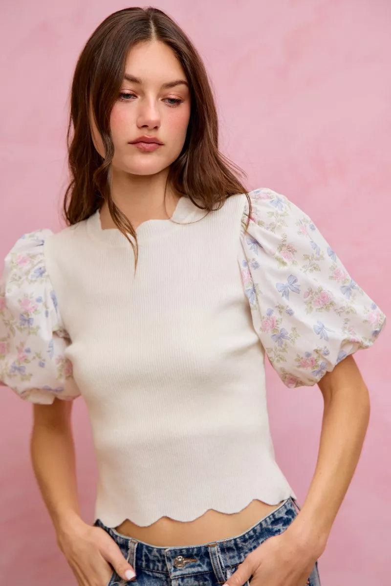 White knit sweater top with floral puff sleeves and scalloped hem at the waist