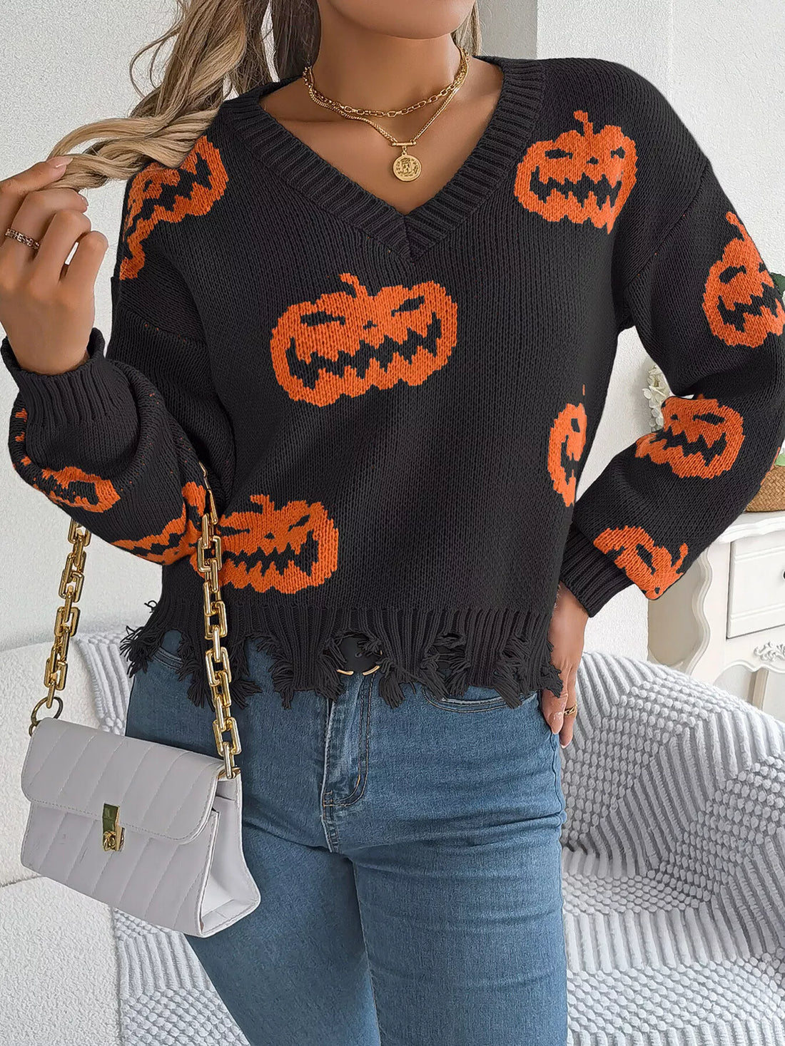 Black knit V-neck pumpkin sweater with orange jack-o’-lantern motifs and distressed fringe hem