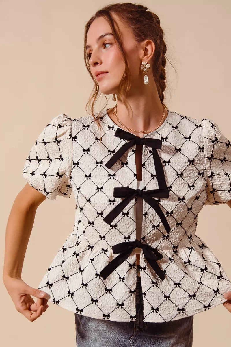 Ivory woven peplum top with black bow tie ribbons and short puff sleeves, angled view.