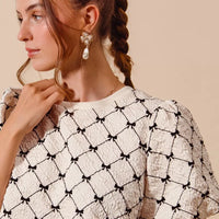 Ivory woven bubble sleeve top with black bow texture pattern, sleeve and neckline close-up