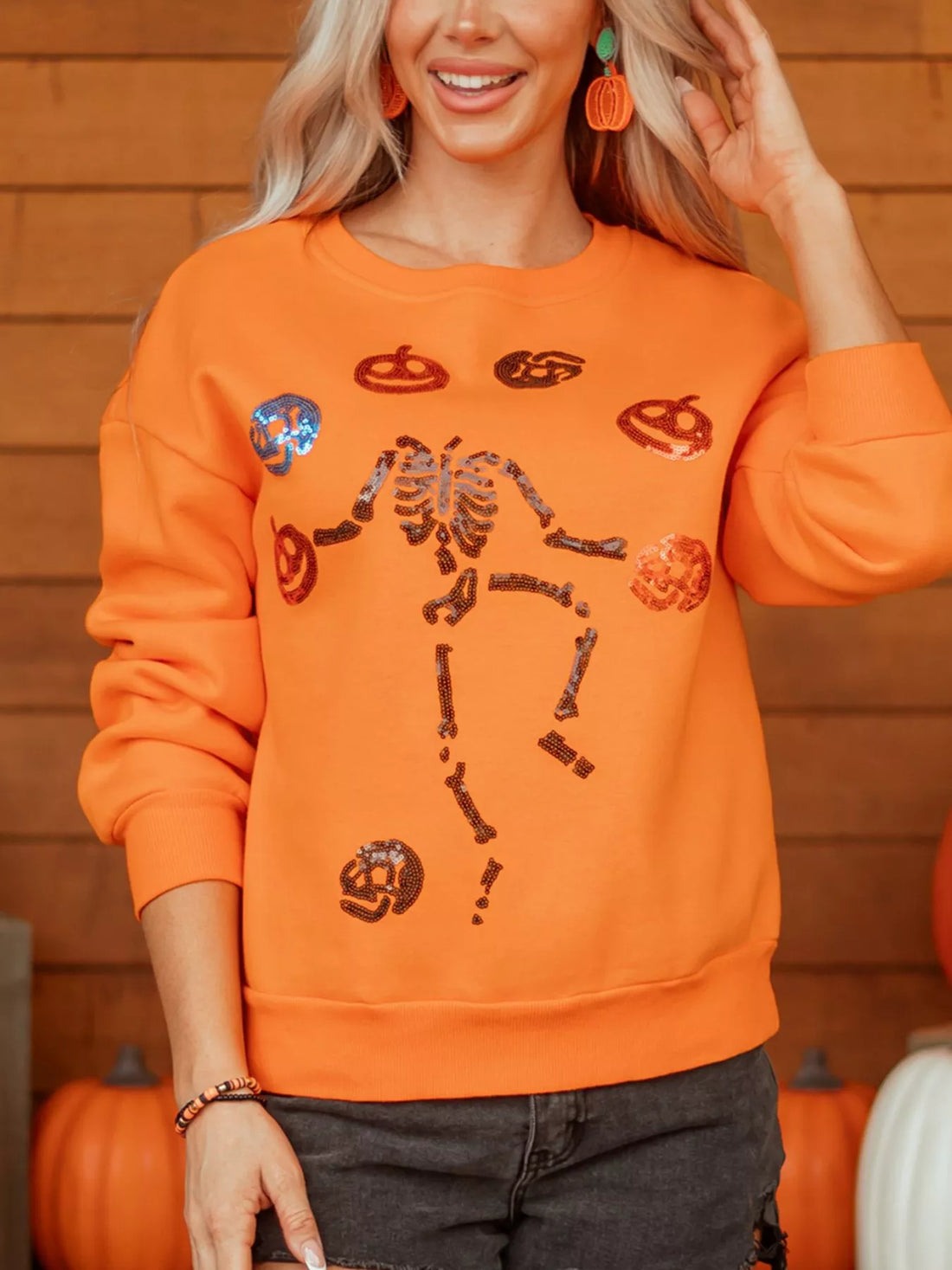 Orange crewneck sweatshirt with sequin skeleton and candy icons, ribbed hem and cuffs