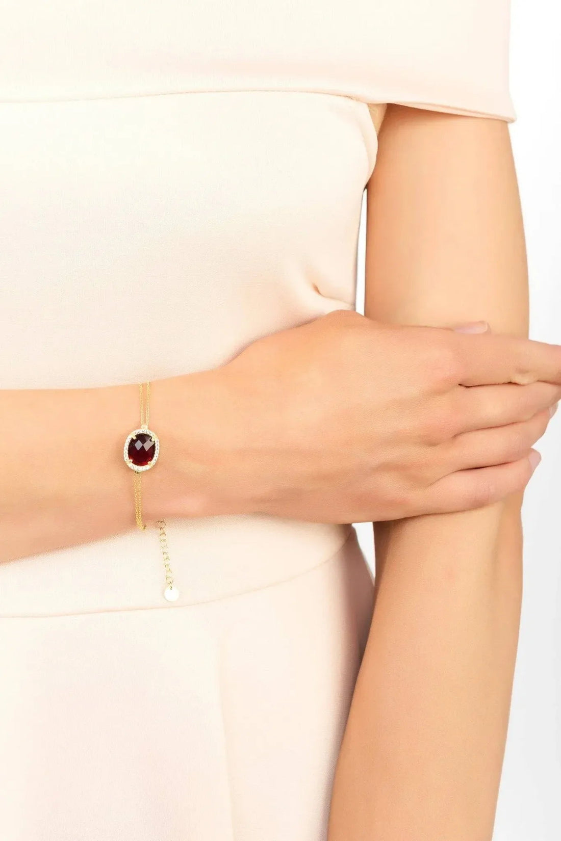 Gold chain bracelet with round red gemstone centerpiece on wrist