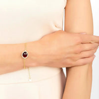 Gold chain bracelet with round red gemstone centerpiece on wrist