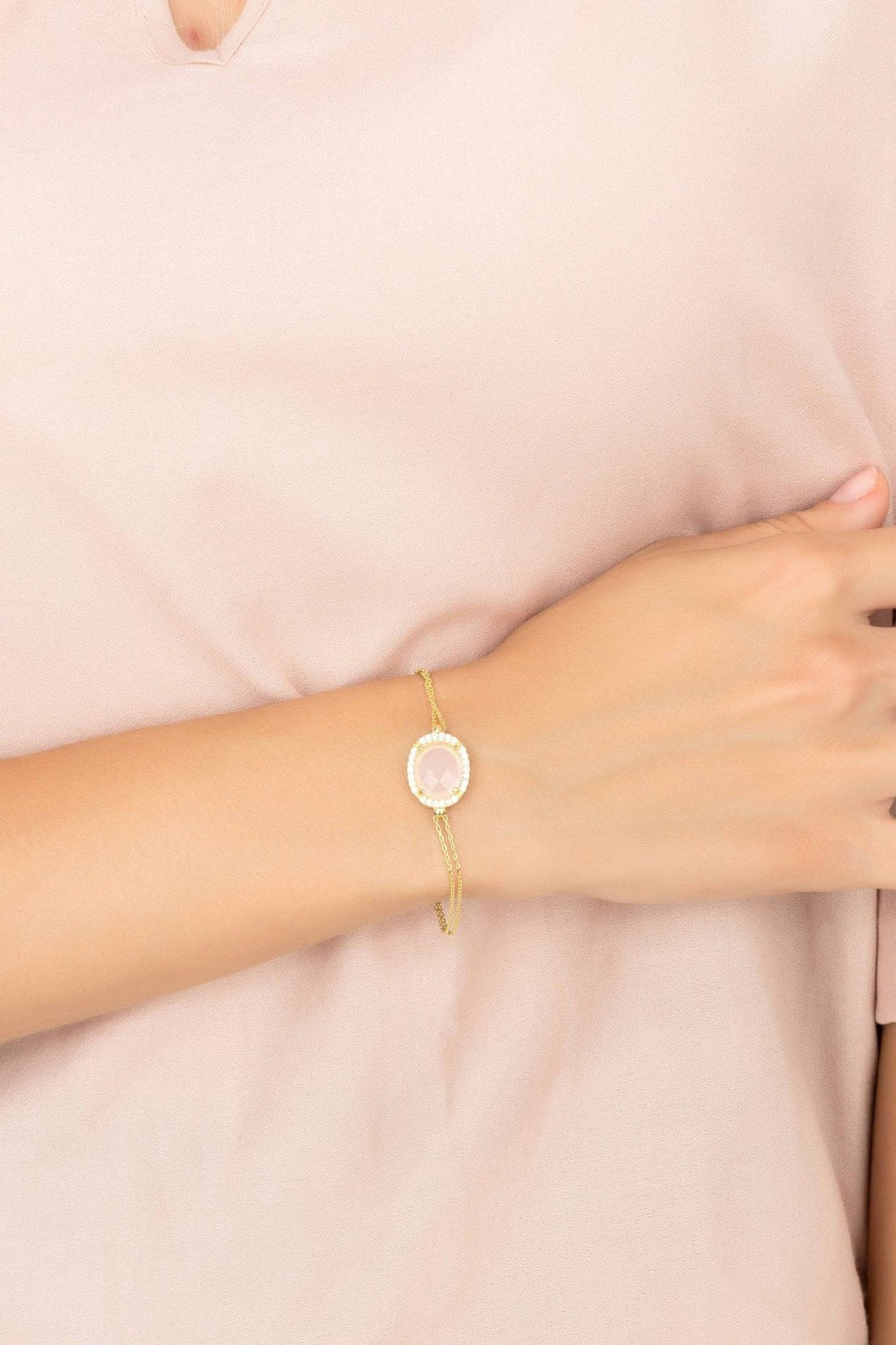 Gold-tone bracelet on wrist with pink oval cabochon charm and link chain