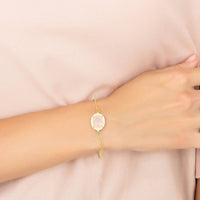 Gold-tone bracelet on wrist with pink oval cabochon charm and link chain
