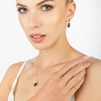 Gold chain necklace with small oval garnet pendant, shown on neckline