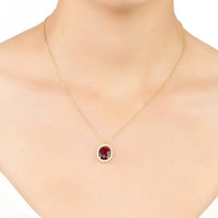 Gold chain necklace with small red oval garnet pendant and clear stone border