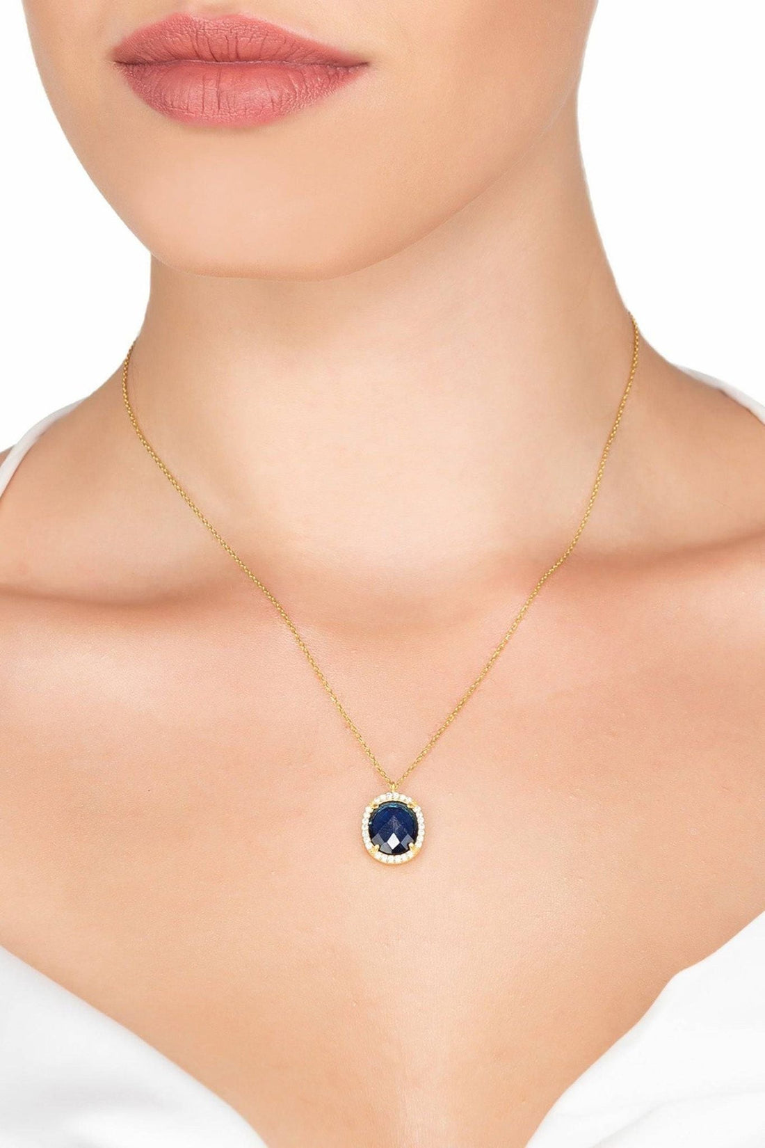 Gold chain necklace with small blue oval pendant at collarbone