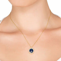Gold chain necklace with small blue oval pendant at collarbone