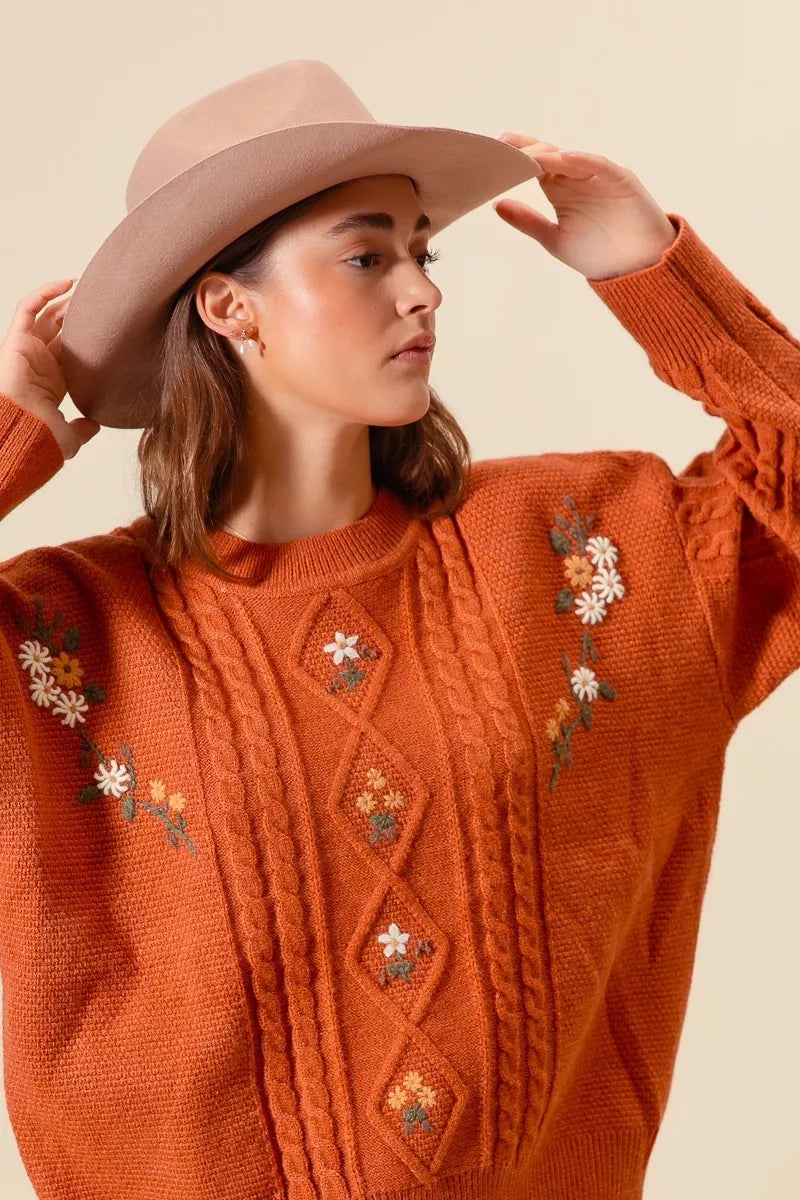 Brick cable-knit sweater detail with embroidered daisy flowers and diamond motifs